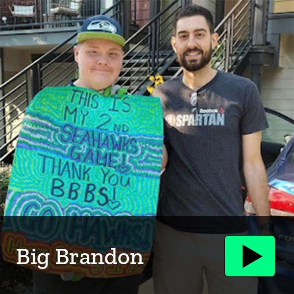 Mentor and mentee going to Seahawks game. Mentee holds sign thanking BBBS for experience.