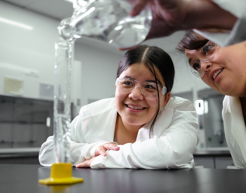 Mentor and mentee conduct science experiment together, smiling. Big Brothers Big Sisters campaign.