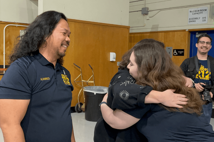 Joseph Alvarico, the robotics team coach, watches as students and supporters embrace after the surprise donation.